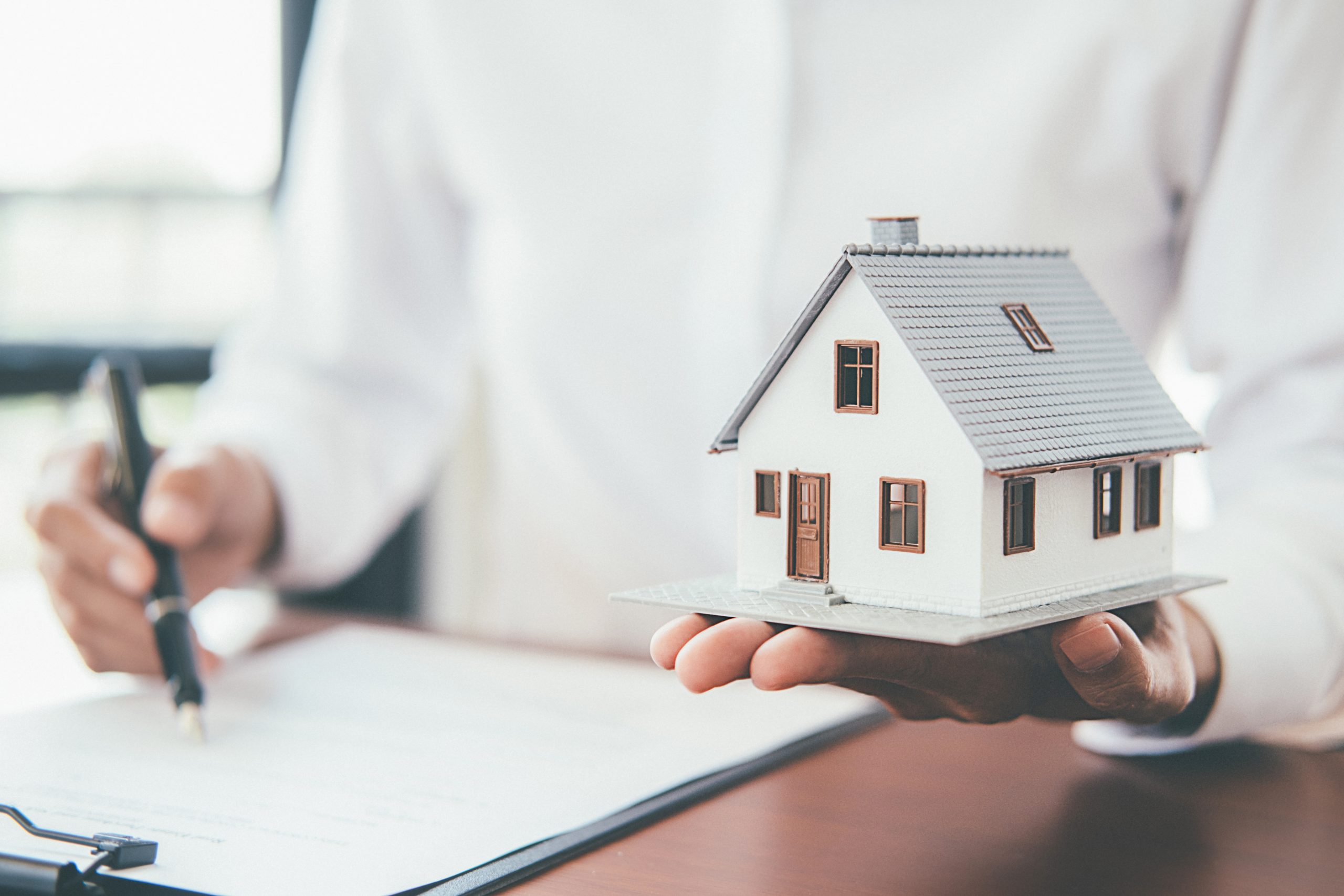assurance-particulierUne assurance adaptée à vos besoins House model with real estate agent and customer discussing for contract to buy house, insurance or loan real estate background.